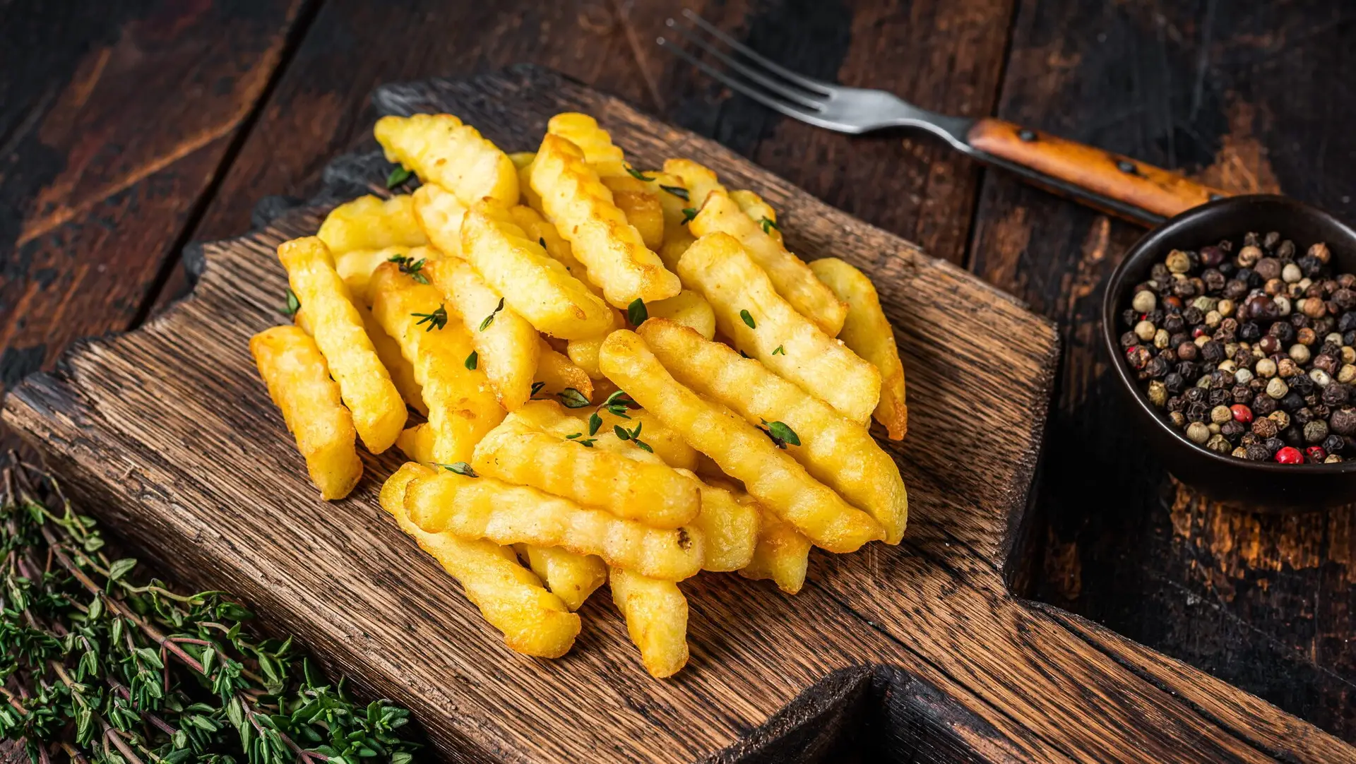 Baked Crinkle French fries potatoes sticks or chips on a wooden board.